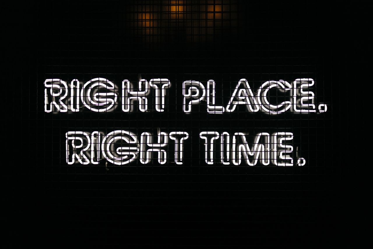 Bright neon sign displaying the text 'Right Place Right Time' against a dark background.