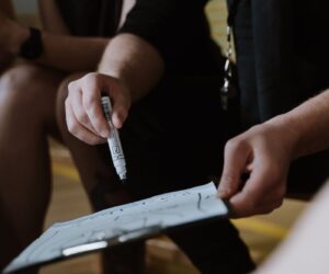 Close-up of a coach planning strategy with a team using a clipboard and marker.