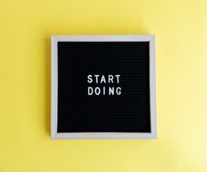 Black message board with 'Start Doing' on a bright yellow background for inspiration.