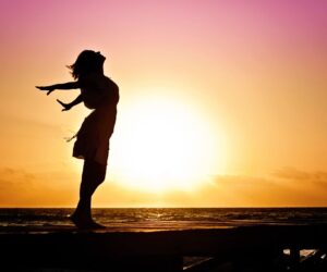 Silhouette of a woman at the beach with arms outstretched against a vibrant sunset backdrop.